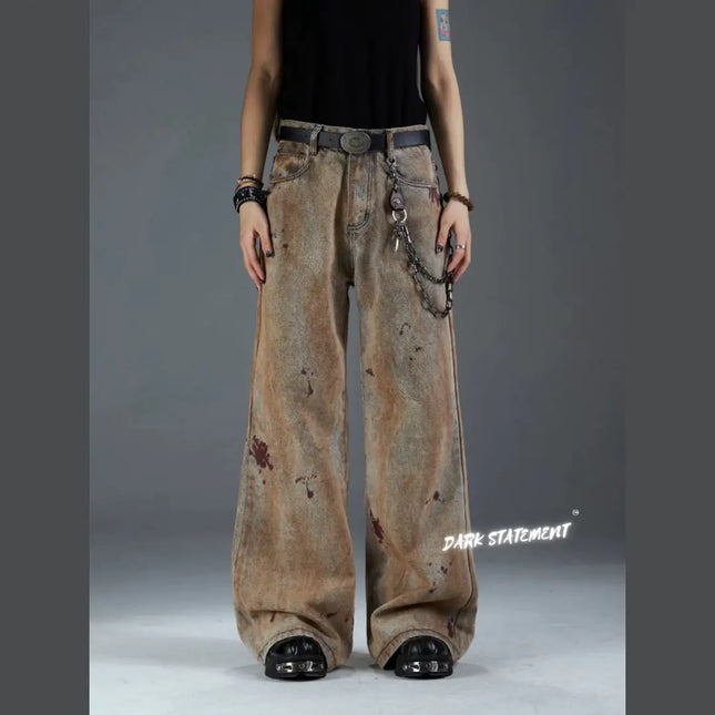 A pair of brown denim jeans with a wide-leg cut, featuring unique earth-like staining and a chain belt.